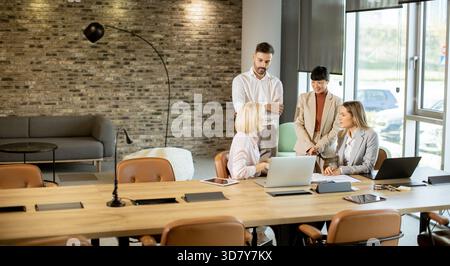 A diverse team engages in a business meeting around a long wooden table. They discuss ideas while laptops and documents are present, creating a collab Stock Photo