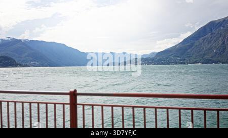 Red railing and rippling lake with distant mountains in soft blurred focus, outdoor; background backplate copyspace calm. Stock Photo