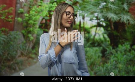 Woman with hand on chest and glasses in a forest path wearing blue shirt and smartwatch; confidence. Stock Photo