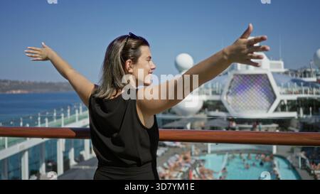 Woman standing with outstretched arms and hands on railing on cruise deck overlooking pool and sea; serenity travel escape. Stock Photo