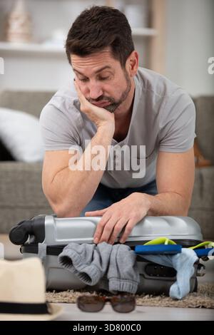 sad male tourist sitting on top of a packed suitcase Stock Photo