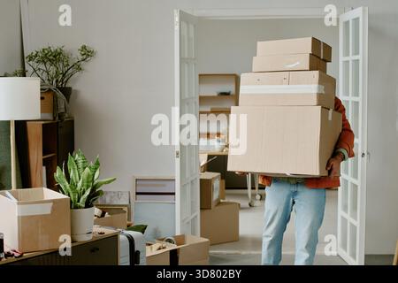 Young Man Carrying Cardboard Boxes While Moving into New Home Stock Photo