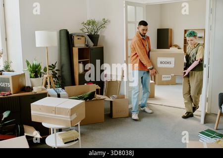 Young Multiethnic Couple Carrying Boxes While Moving into New Apartment Stock Photo