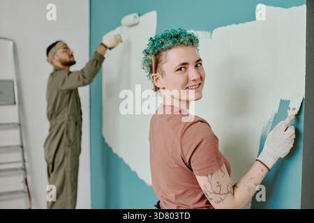 Young Caucasian Woman Smiling While Painting Wall with Young Man Renovating Stock Photo
