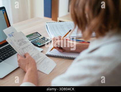 Woman checking paper bills while calculating expenses at home. Over-shoulder view of pencil and calculator. Home budget, smart money management and pe Stock Photo