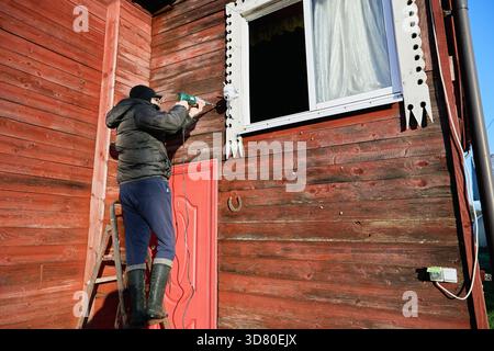Creating opening for security camera wiring, technician operates power drill to bore hole in exterior wall, installer concentrates on drilling process Stock Photo