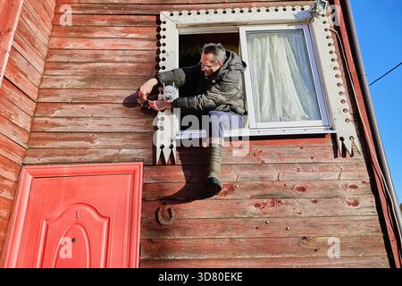 Linking power lines as installer attaches DC jack male to DC jack female during surveillance camera setup on rural home facade. Stock Photo