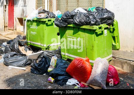 Overflowing green dumpsters surrounded by garbage bin bags and litter scattered on the pavement in an urban alley malaysia Stock Photo
