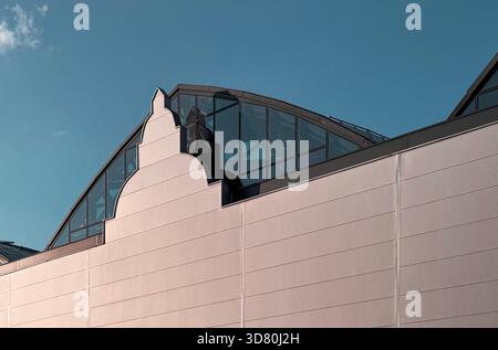 Sleek modern architecture with a curved glass roofline and clean facade against a clear blue sky, showcasing contemporary design and reflections. Stock Photo