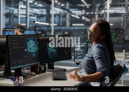Technician in data center office using AI powered tech to run simulations. African american IT expert coding cognitive computing algorithms to extract insights from data and automate rigs Stock Photo