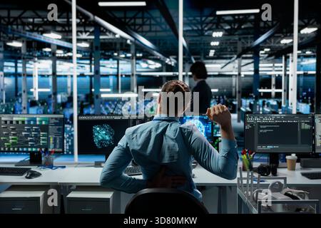Data center technician stretching back to combat sedentary fatigue after working long hours at desk. Server farm employee fixing incorrect posture at workstation, alleviating discomfort Stock Photo