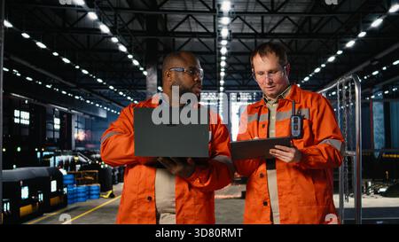 Diverse workers using devices to manage steel production tasks, surrounded by metal machinery and fabrication tools. Professional engineering and manpower on the factory floor. Stock Photo