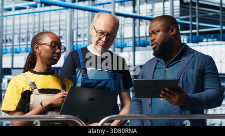 Manager overseeing smart factory, giving instructions to engineers testing automated systems. Industry 4.0 industrial plant supervisor tasking employees with identifying bottlenecks, camera A Stock Photo