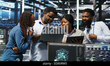 Portrait of smiling data center specialists collaborating in server facility, using node tree software to analyze datasets. Happy team using visual programming to improve gear performance, camera B Stock Photo