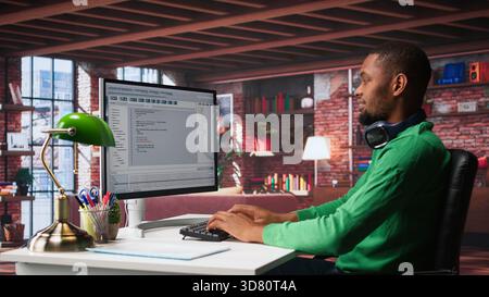 Tech savvy black engineer developing secure online program at home. Surrounded by binary data, freelancer works on interface design, script optimizations and network systems. Camera B. Stock Photo