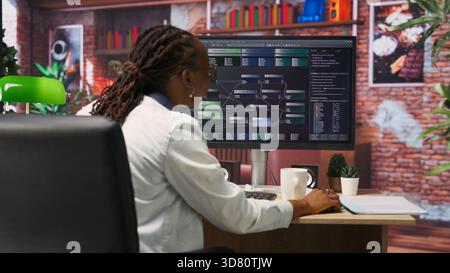Teleworking computer scientist at home using PC to develop artificial intelligence self learning algorithms. African american woman working with AI machine learning software on PC, camera B Stock Photo