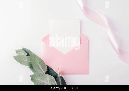 Pink envelope with blank card and ribbon on white background. Holiday greeting card, invitation, wedding concept. Top view, flat lay, mockup. Stock Photo