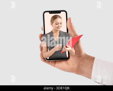 Hand holding mobile phone with female business speaker on screen against light background Stock Photo