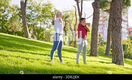 Senior couple stretching arms exercising outdoors in a park Stock Photo