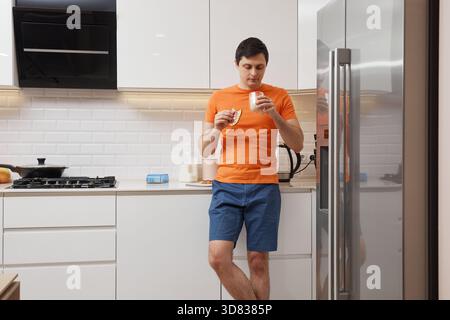 Young man standing in a modern kitchen, eating a sandwich and drinking milk Stock Photo