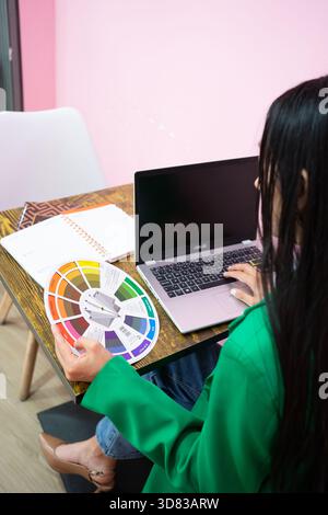 Woman designer choosing colors, using a color wheel and laptop at her workspace Stock Photo