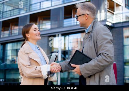 Happy business partners handshake outdoors. Diverse team seals deal outside modern office. Success, agreement and collaboration concept Stock Photo