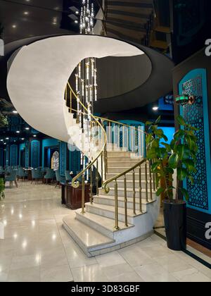 Elegant spiral staircase with a brass railing and modern chandelier Stock Photo