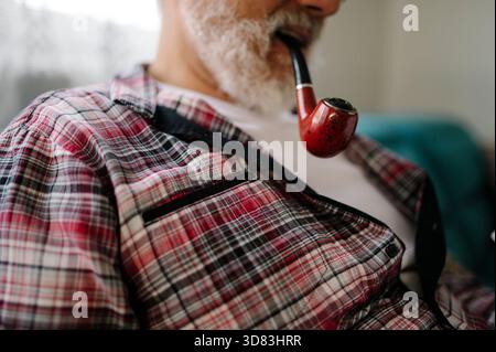 Elder man enjoys pipe smoking while relaxing indoors Stock Photo