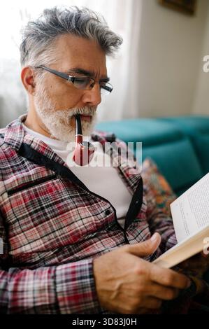 Older man reading a book while enjoying a pipe Stock Photo