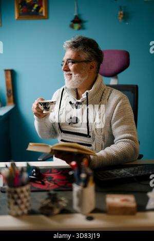 Senior man enjoys tea while reading a book Stock Photo
