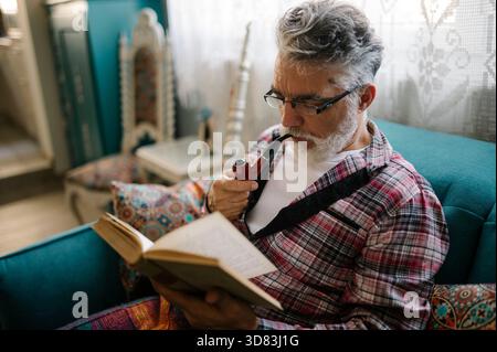 Senior man enjoys reading book while relaxing on sofa Stock Photo