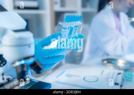 Two female scientists in white lab coats working together in a bright laboratory with microscopes, glassware, and blue test tubes, representing teamwo Stock Photo
