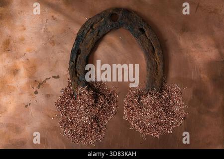 Old rusty horseshoe on a copper metal surface with two piles of copper shavings placed at the ends. Luck and craftsmanship. Stock Photo