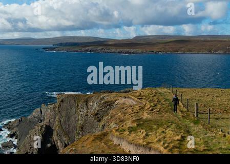 Woman walking along the Shetland coastline Stock Photo