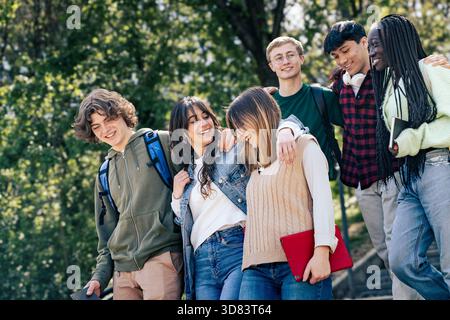 A group of diverse young students walking together outdoors on campus, smiling and enjoying a cheerful moment of friendship and connection. Stock Photo