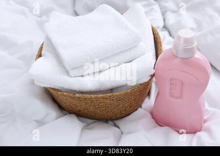 Laundry basket with folded towels and bottle of detergent on bed linens, closeup Stock Photo