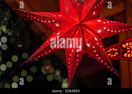 A glowing red paper star lantern hanging at a christmas market stall, illuminated with warm light. Stock Photo