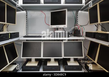 Multiple outdated desktop computers, including LCD monitors and horizontal processing units, arranged on white metal shelving. Stock Photo