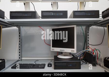Multiple outdated desktop computers, including LCD monitors and horizontal processing units, arranged on white metal shelving. Stock Photo