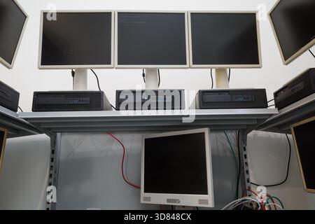 Multiple outdated desktop computers, including LCD monitors and horizontal processing units, arranged on white metal shelving. Stock Photo