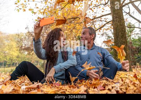 Mature couple making silly faces and taking a selfie among falling autumn leaves in a park Stock Photo