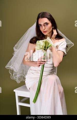 A young bride elegantly poses in a simple yet stunning gown, holding serene flowers. Stock Photo