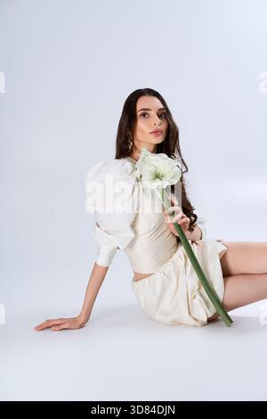 A stunning bride elegantly poses with a delicate flower, exuding grace and joy in a studio. Stock Photo