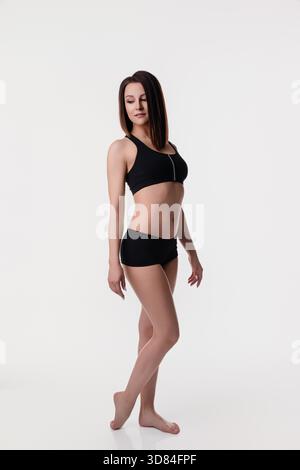 A woman stands gracefully in black athletic wear, showcasing her toned physique. She poses with confidence, highlighting both her athleticism and elegance. || Model released Stock Photo