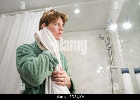 Young caucasian man in green bathrobe dries his face with towel. Daily personal care routine, self-care. Morning Shaving Routine Stock Photo