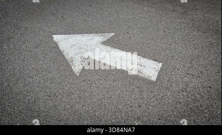 White painted arrow on asphalt road surface, representing direction and navigation in transportation contexts. Stock Photo