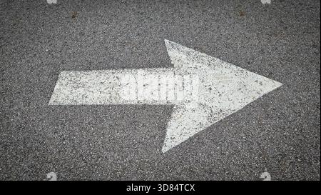 White painted arrow on asphalt road surface, representing direction and navigation in transportation contexts. Stock Photo