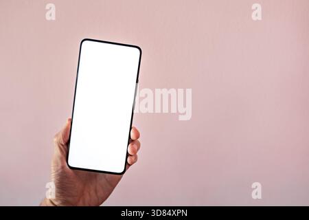 smartphone with blank screen held in hand. hand holding blank mobile screen placed on table, frameless modern design. Stock Photo