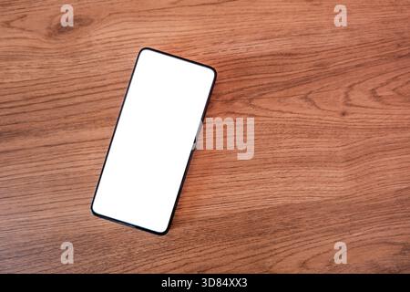 smartphone with blank screen on desk. blank mobile screen placed on table, frameless modern design. Stock Photo