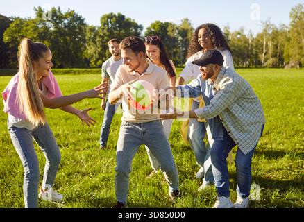 Happy diverse group of young people friends playing ball together in park, sunny outdoor, excited Stock Photo